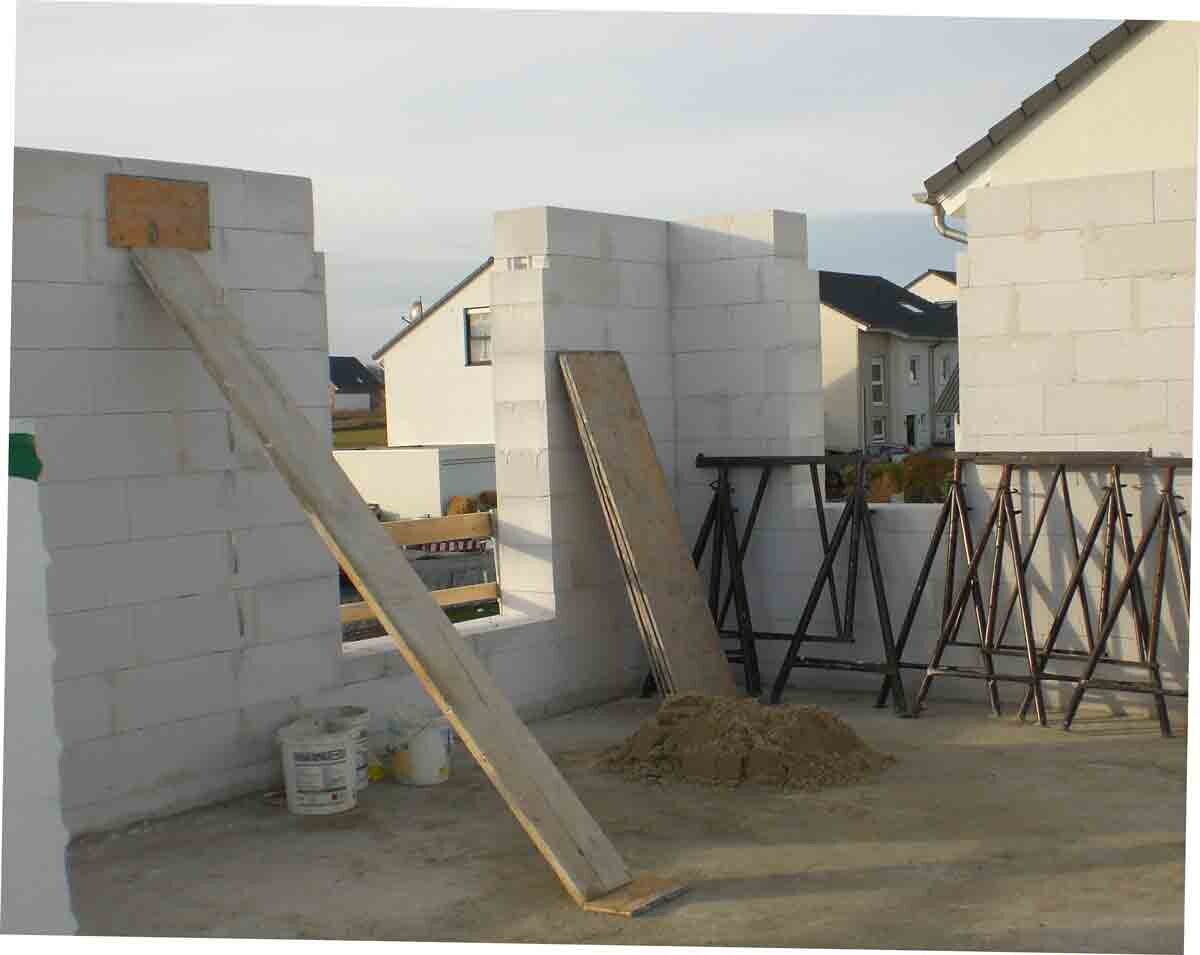 Baustelle mit weißen Betonblockwänden, Holzplanken, Gerüsten und Sandhaufen