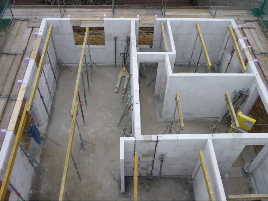 Innenaufnahme eines unfertigen Rohbaus: weiße Betonblockwände, Holzträger, Gerüste im Bau.