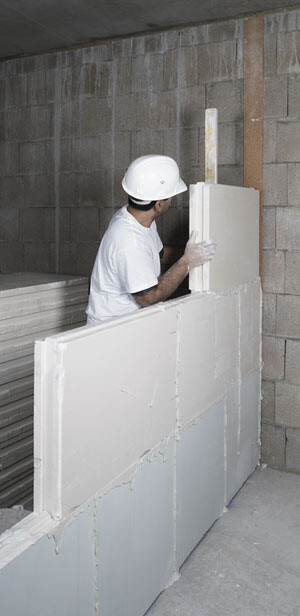 Bauarbeiter mit Schutzhelm montiert Styropor-Wandbaustein im Rohbau