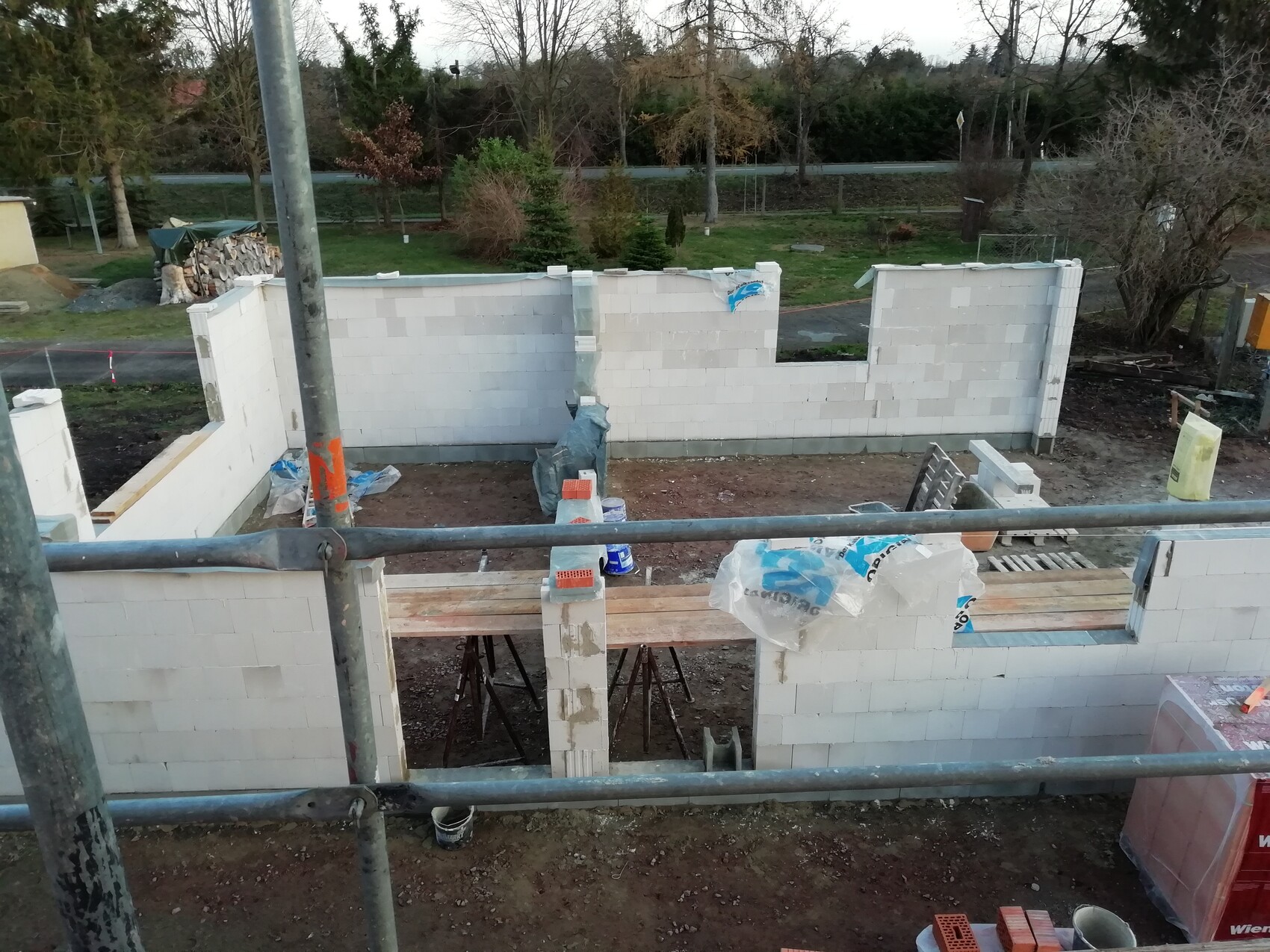 Baustelle: Wand aus weißen Porenbetonblöcken; Gerüststangen und Baumaterialien im Vordergrund.