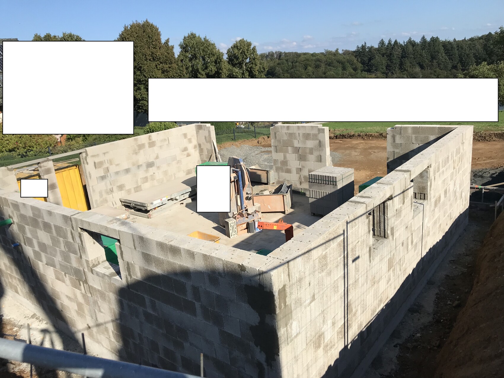 Baustelle mit unfertigem Mauerwerk aus Betonstein, Paletten, Baumaterialien und Baugeräten.