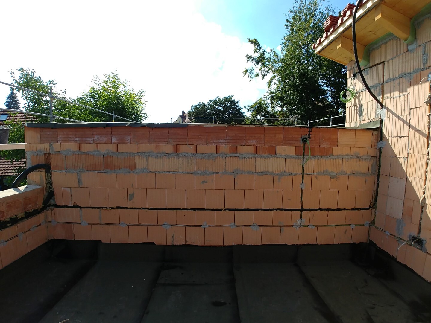 Unverputzte Ziegelwand auf Baustelle mit Kabeln und Baumaterialien, Blick auf Baufläche