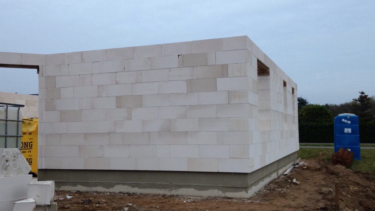 Rohbau eines Gebäudes aus weißen Betonblöcken; Fundament sichtbar, blaue Tonne rechts.