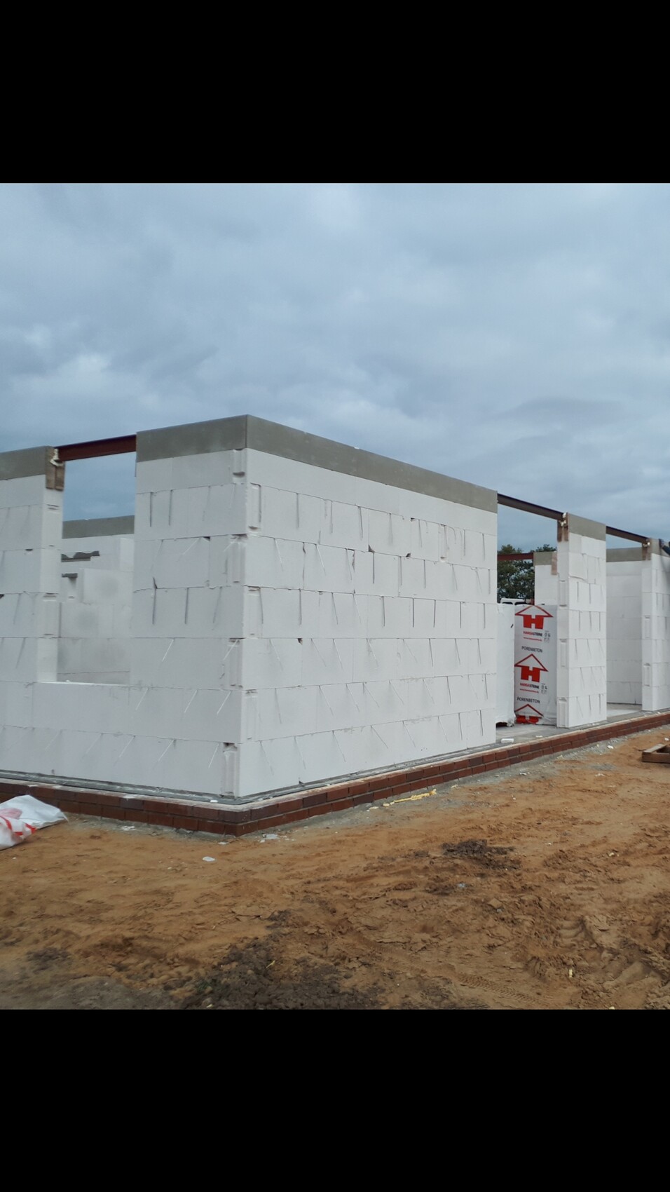Weisse Rohbauwaende aus Bloecken auf einer Baustelle, Erdreich und Fundament sichtbar