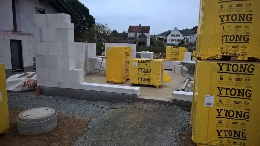 Baustelle: weiße Ytong-Steine stapeln, gelbe Ytong-Verpackungen, unfertiger Mauerbau
