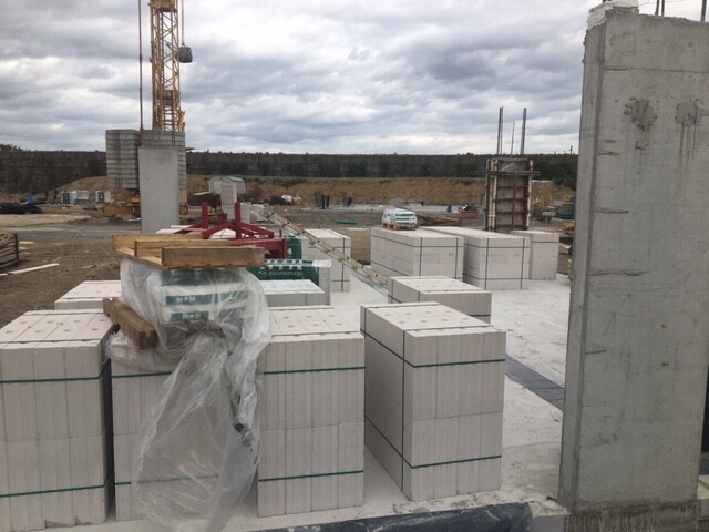 Baustelle mit gestapelten weißen Baublöcken auf Paletten, Kran im Hintergrund.
