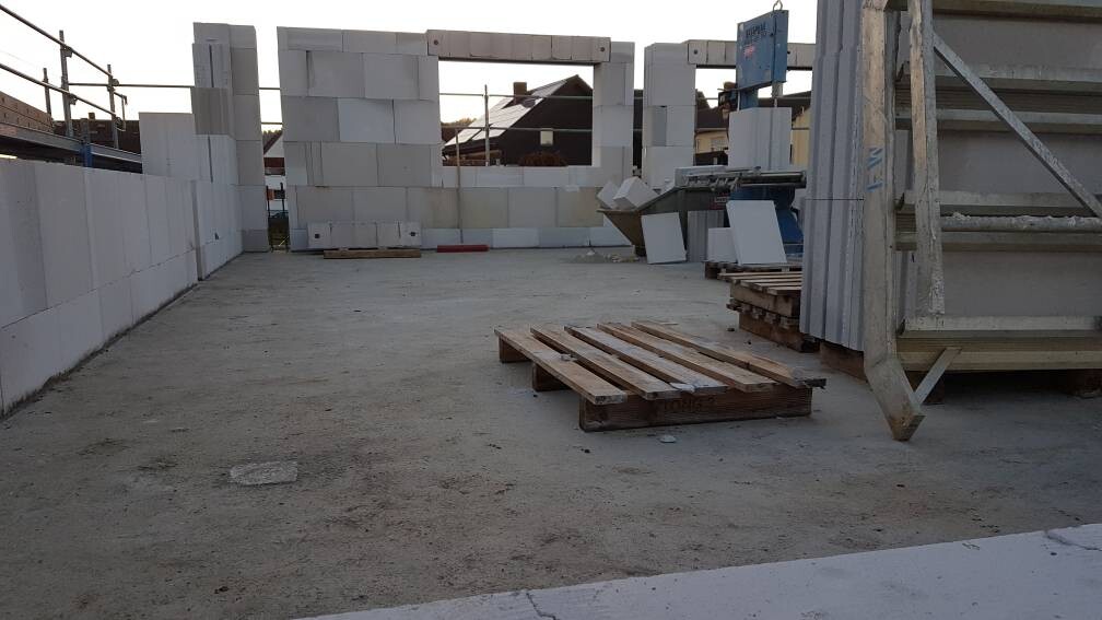 Baustelle mit weißen Betonblöcken als Mauer, Paletten und Baugeräten auf Betonboden
