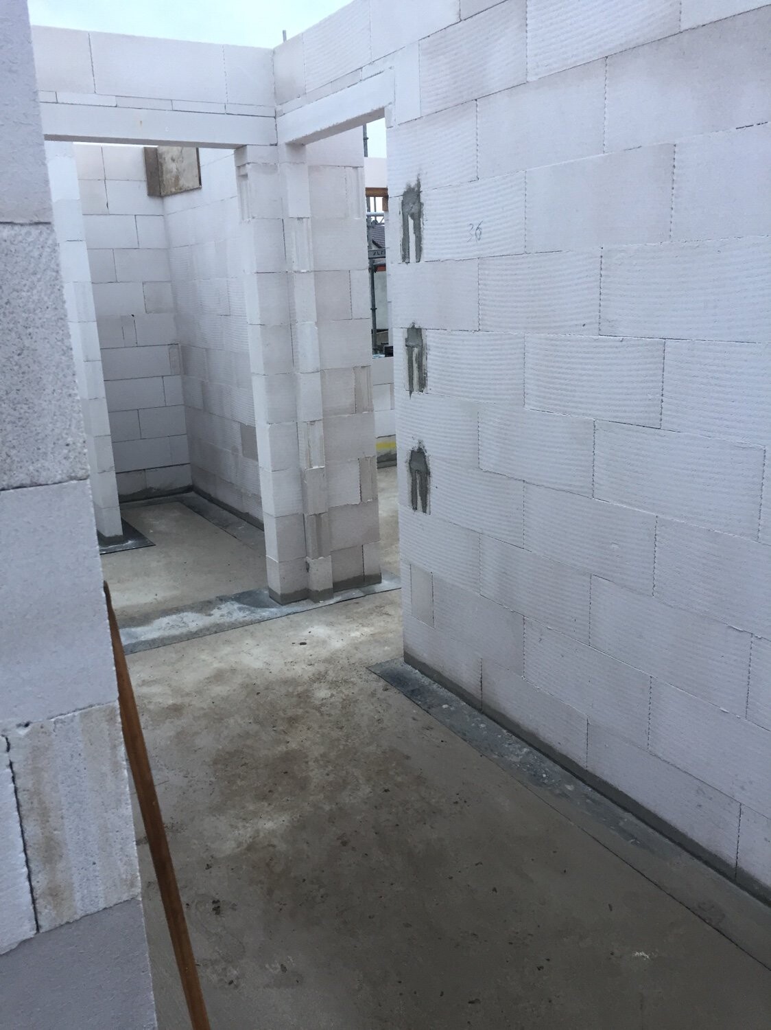 Unfertiger Innenbereich aus weißen Betonblöcken mit Türdurchgängen und Betonboden.