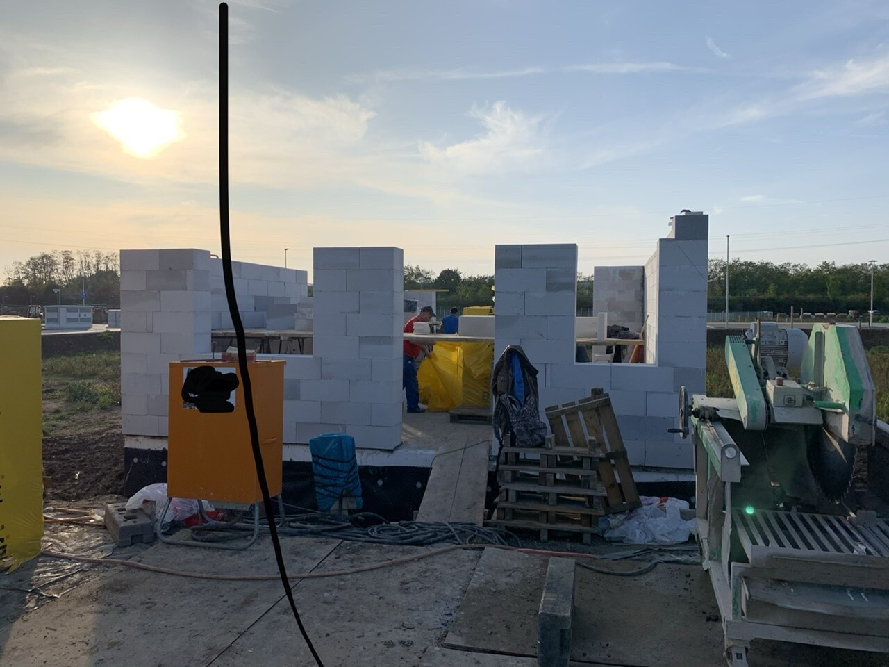 Baustelle mit weißen Blockwänden, Arbeiter baut Mauer im Freien bei Sonnenuntergang.