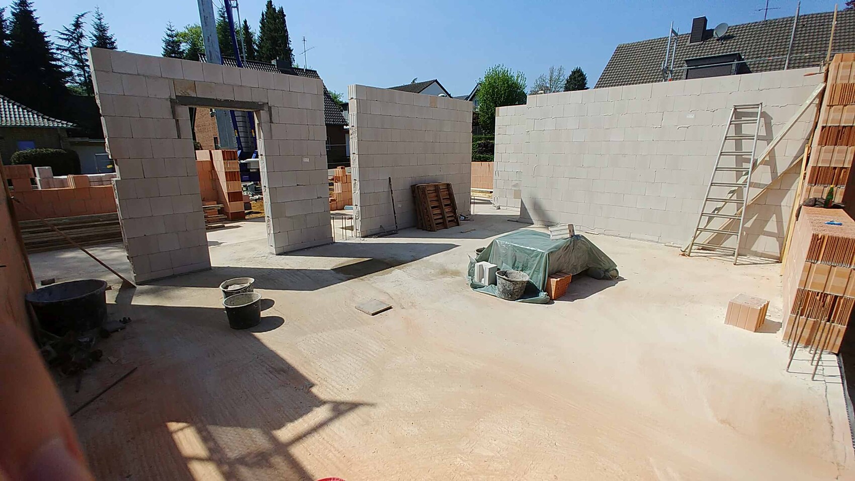 Baustelle mit hellen Betonblockwänden, offener Innenraum, rechte Leiter und Bauteile in der Mitte