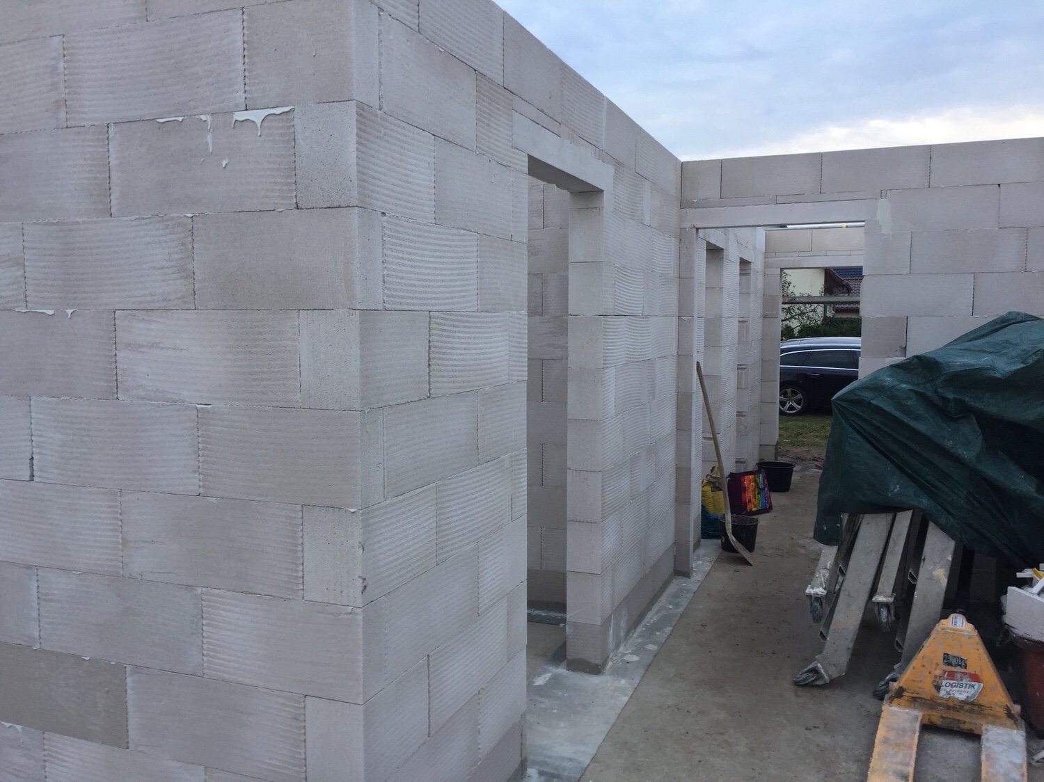 Rohbau aus hellgrauen Betonblöcken mit Türöffnungen, Bauwerk im Bau, Werkzeuge und Auto im Hintergrund