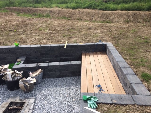 Unfertige Terrasse: schwarze Steinblöcke als Umrandung, Holzdeck, Kiesboden, Werkzeuge und Handschuhe.