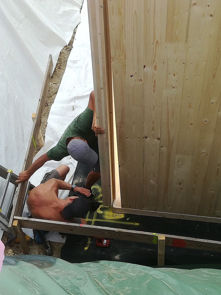 Zwei Bauarbeiter arbeiten an einer Holzverkleidung einer Rohbauwand auf einer Baustelle.