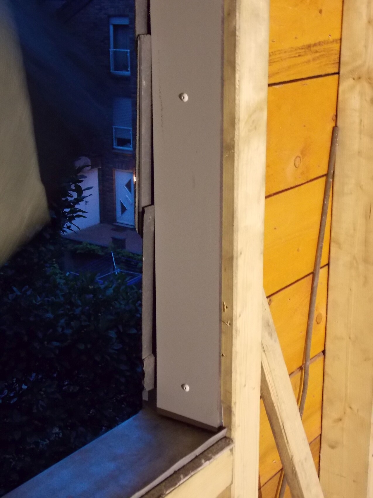 Baustelle mit Holzrahmenkonstruktion einer Außenwand, Metallplatte und blauem Abendlicht.