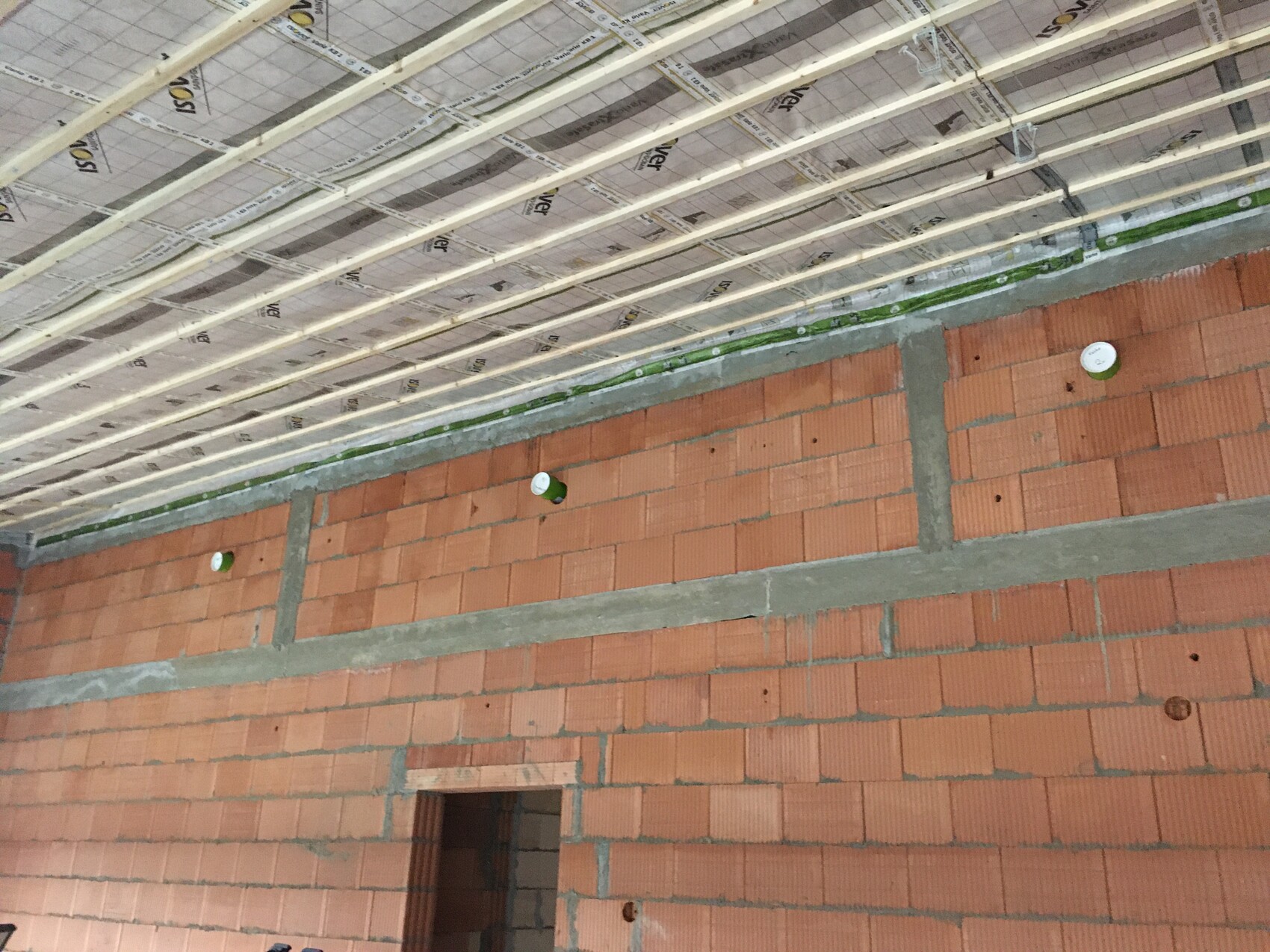 Rohbauzimmer mit roter Backsteinwand, Decke aus Holzlatten, grüne Rohre und weiße Abdeckkappen.