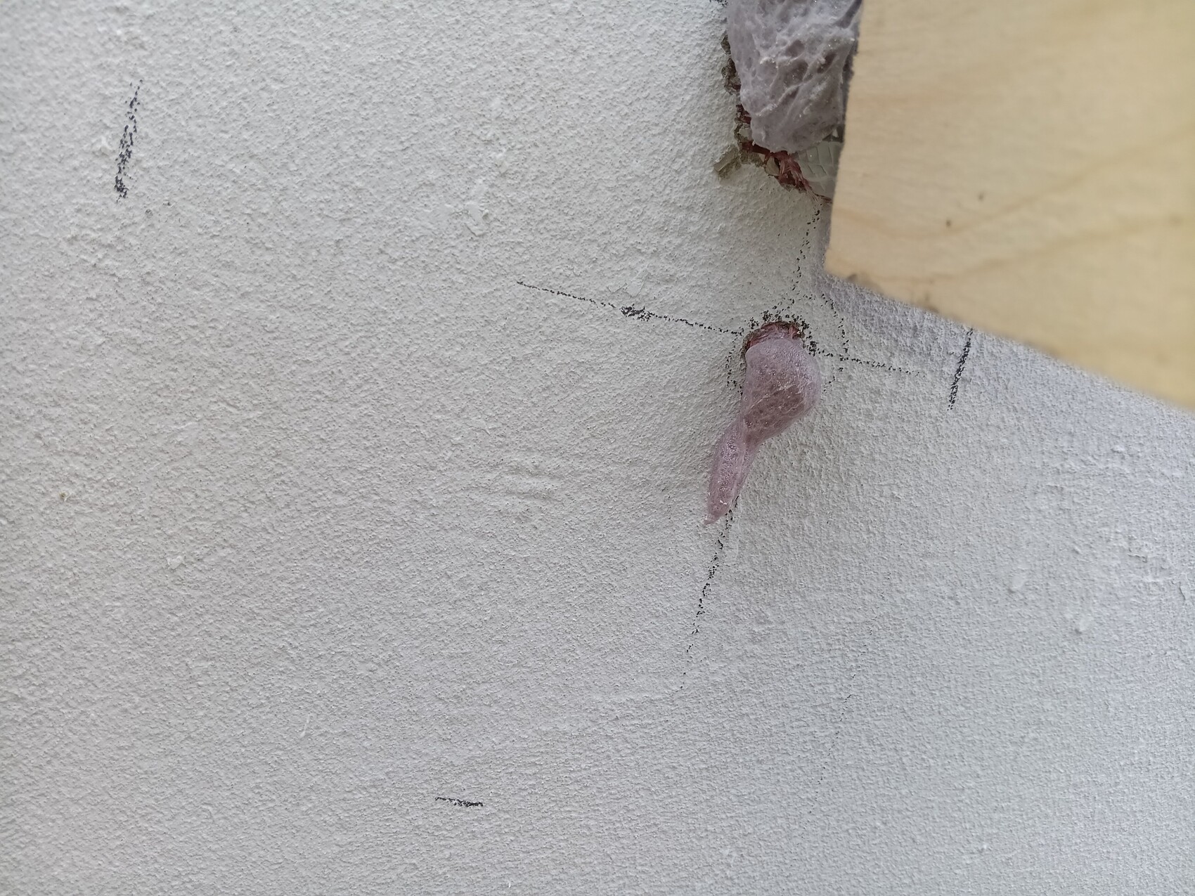 Nahaufnahme einer rauen verputzten Wand mit Rissen; aus einem Loch ragt pinkfarbener Dichtstoff.