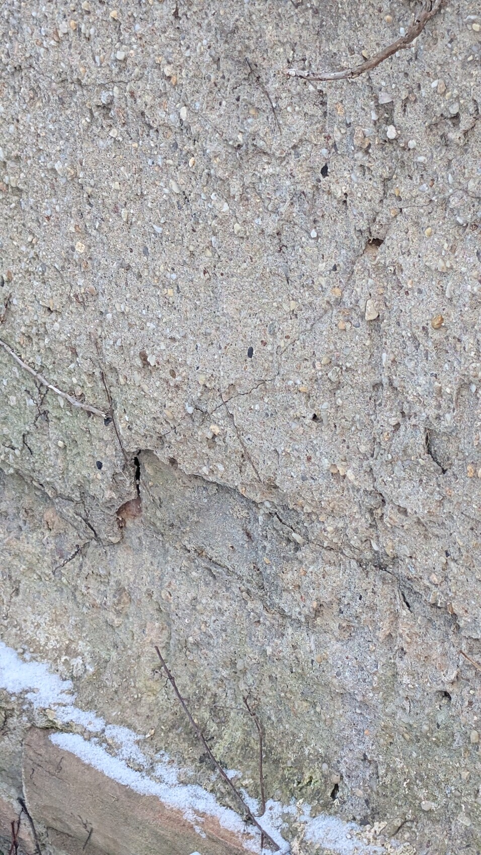 Nahaufnahme einer rauen Betonwand mit Kieseln, Rissen und Verputz