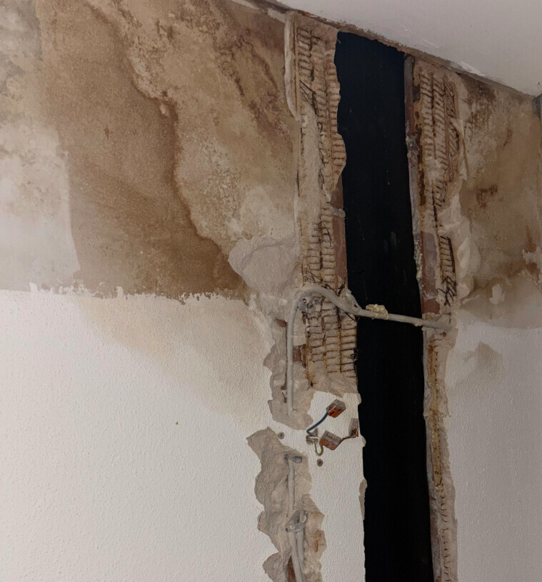 Freigelegte Wandöffnung mit Ziegeln, Putzresten, losen Kabeln und dunklem Spalt dahinter