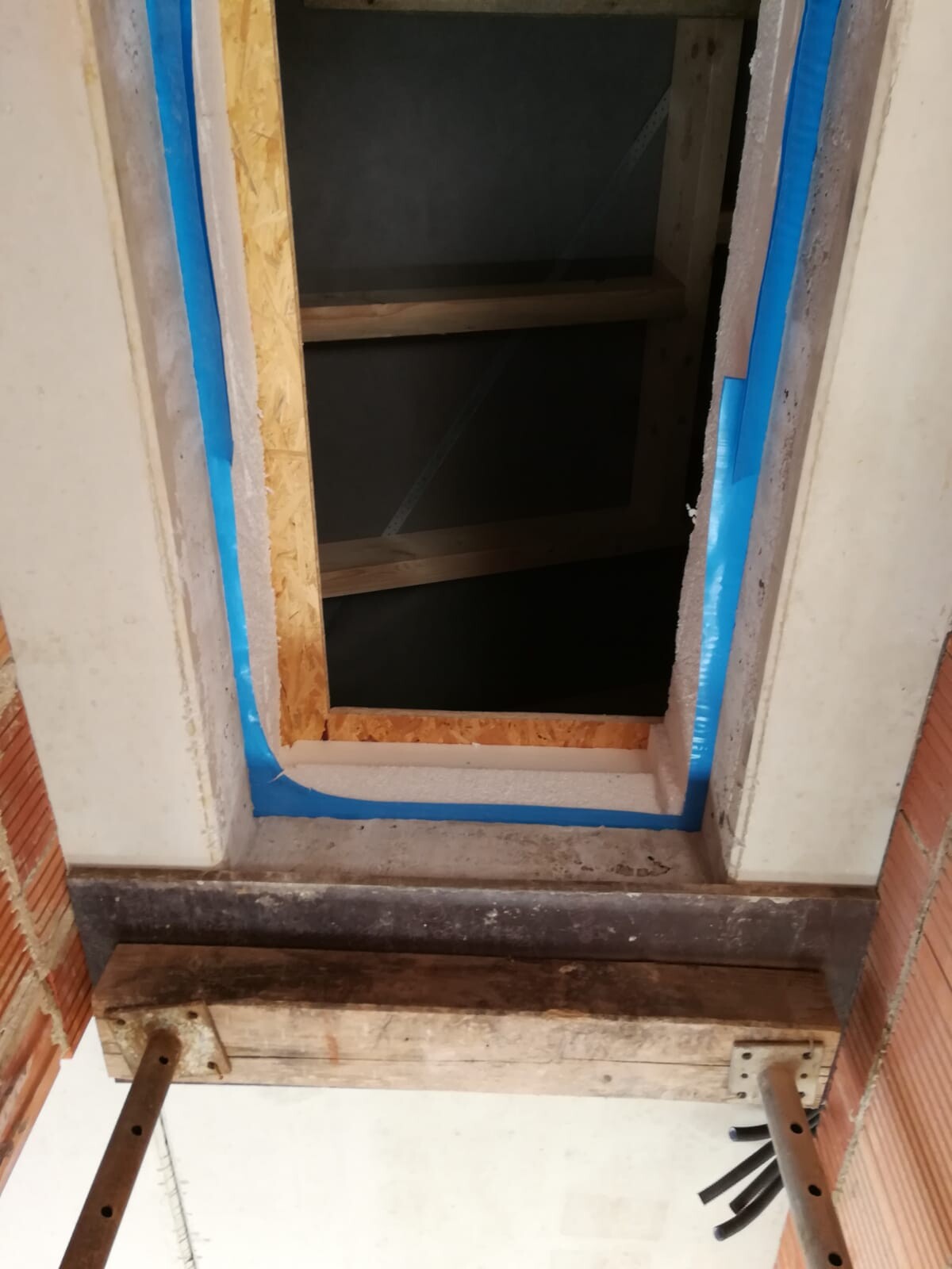 Holzrahmenöffnung in Wand mit blauem Malerband, OSB-Bretter und Metallstützen