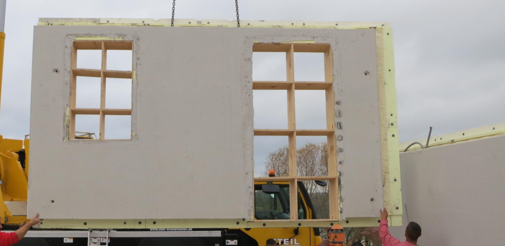 Großes Wandpaneel mit zwei Fensteröffnungen wird auf Baustelle von Kran montiert