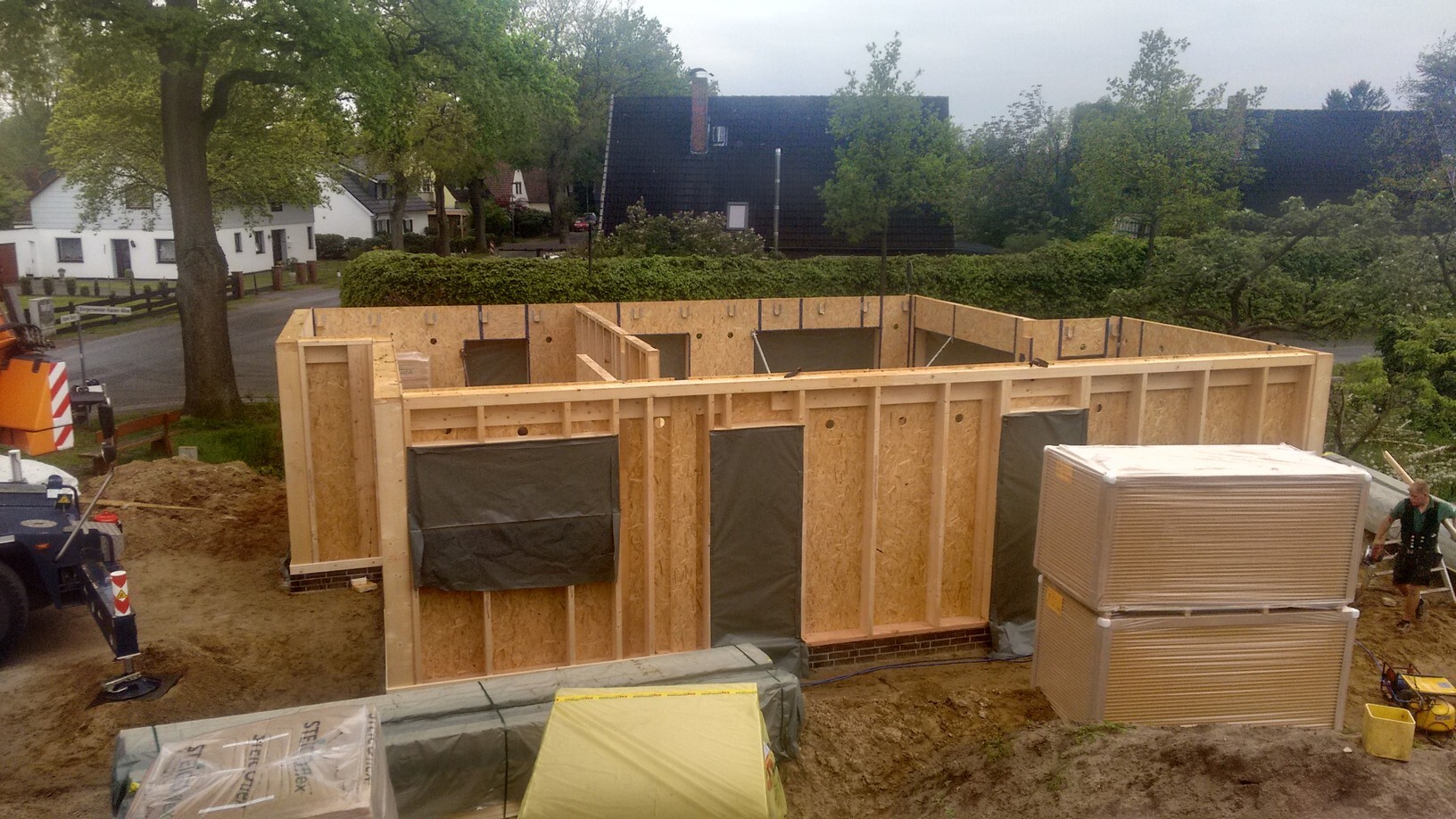 Holzrahmenhaus-Bau: OSB-Wände, Fensteröffnungen, Dämmplattenstapel auf Baustelle.
