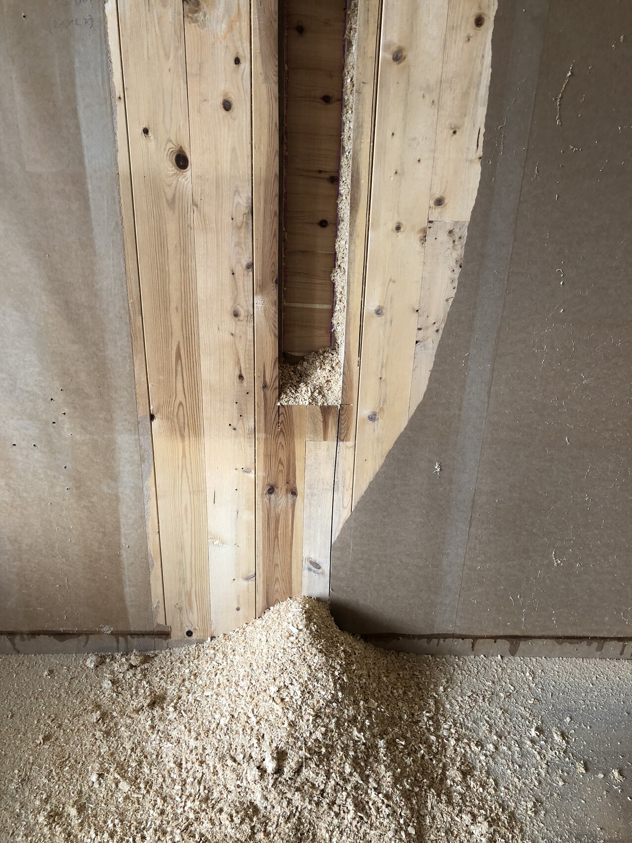 Innenansicht einer Holzwand mit schmaler Öffnung und Sägemehl am Boden.