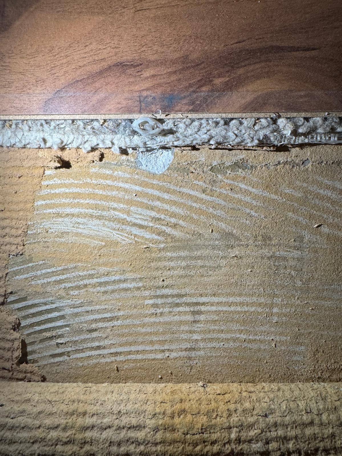 Detail einer Wandkonstruktion: Holzplatte oben, grauer Dämmstoffstreifen und sandiger Putz.