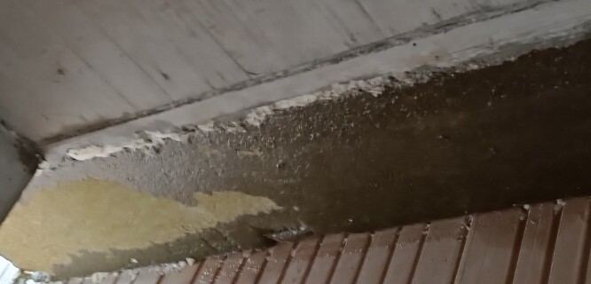 Nahaufnahme einer beschädigten Boden- und Wandkante mit abgeplatztem Putz.
