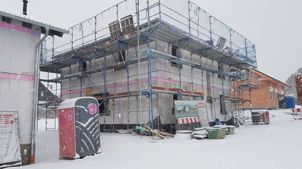 Baustelle mit Gerüst, verschneiter Neubau; portable Toilette vorne