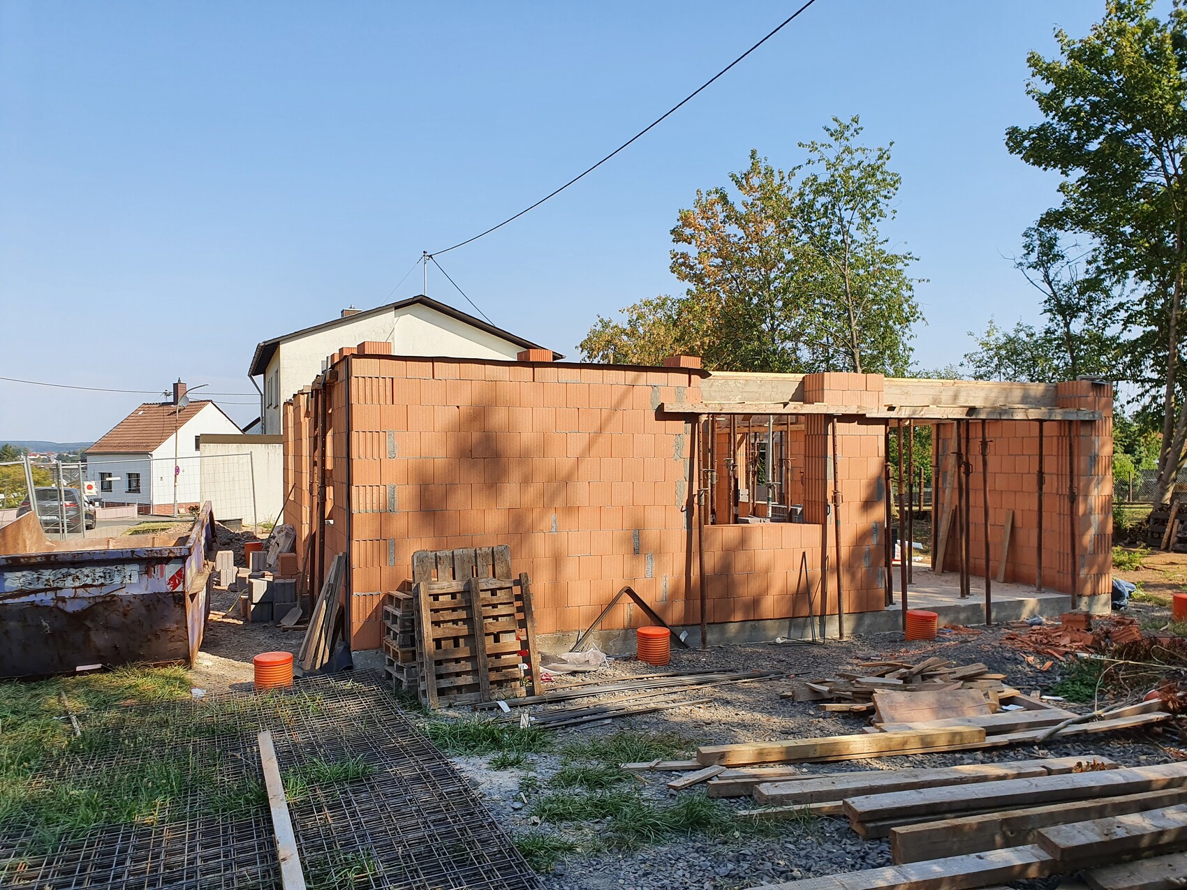 Rohbau eines roten Ziegelhauses mit Holzbalken, Paletten und Bauholz auf Baustelle