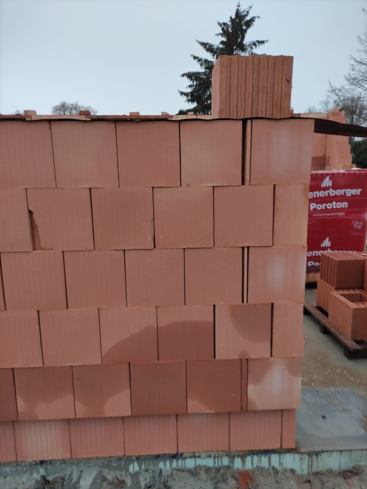 Stapel roter Ziegelsteine auf einer Baustelle, Paletten mit Verpackung im Hintergrund.