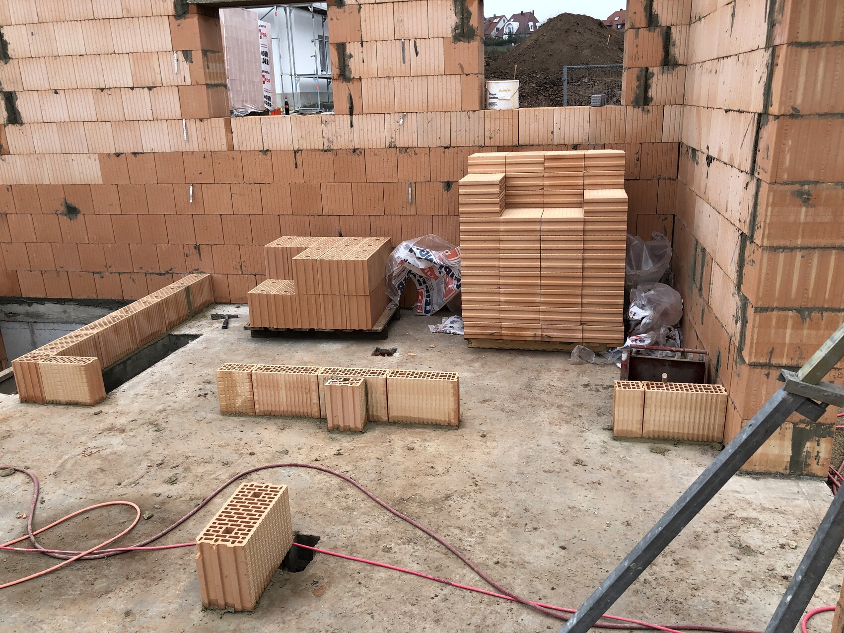 Baustelle mit roten Ziegeln: gestapelte Ziegel auf Paletten und Erdhaufen.