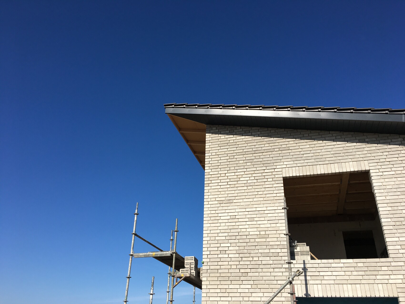 Bau eines Hauses: helle Ziegelwand, große Fensteröffnung, Gerüst im Vordergrund, blauer Himmel