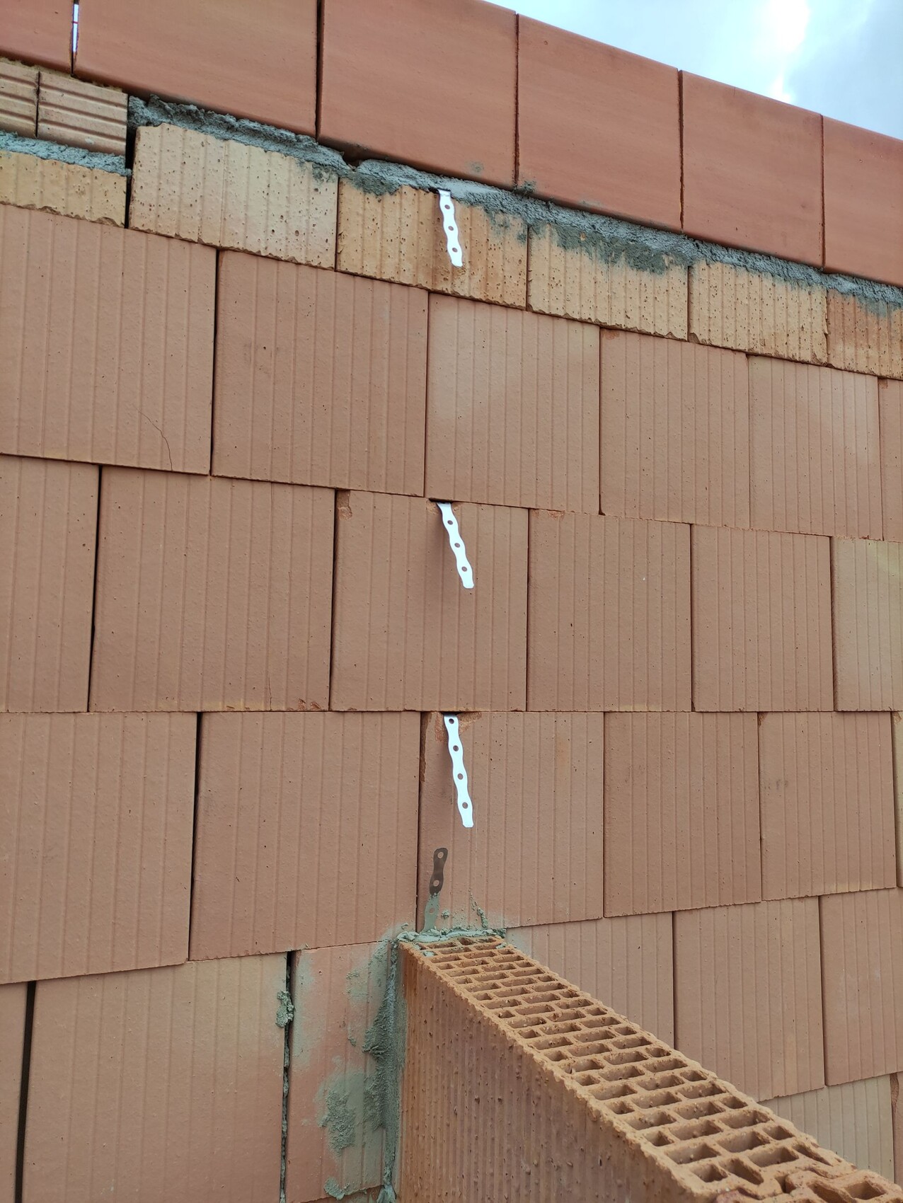 Rote Ziegelwand im Bau mit weißen Wandankern, Mörtelreste; unten liegt ein Hohlblockziegel.