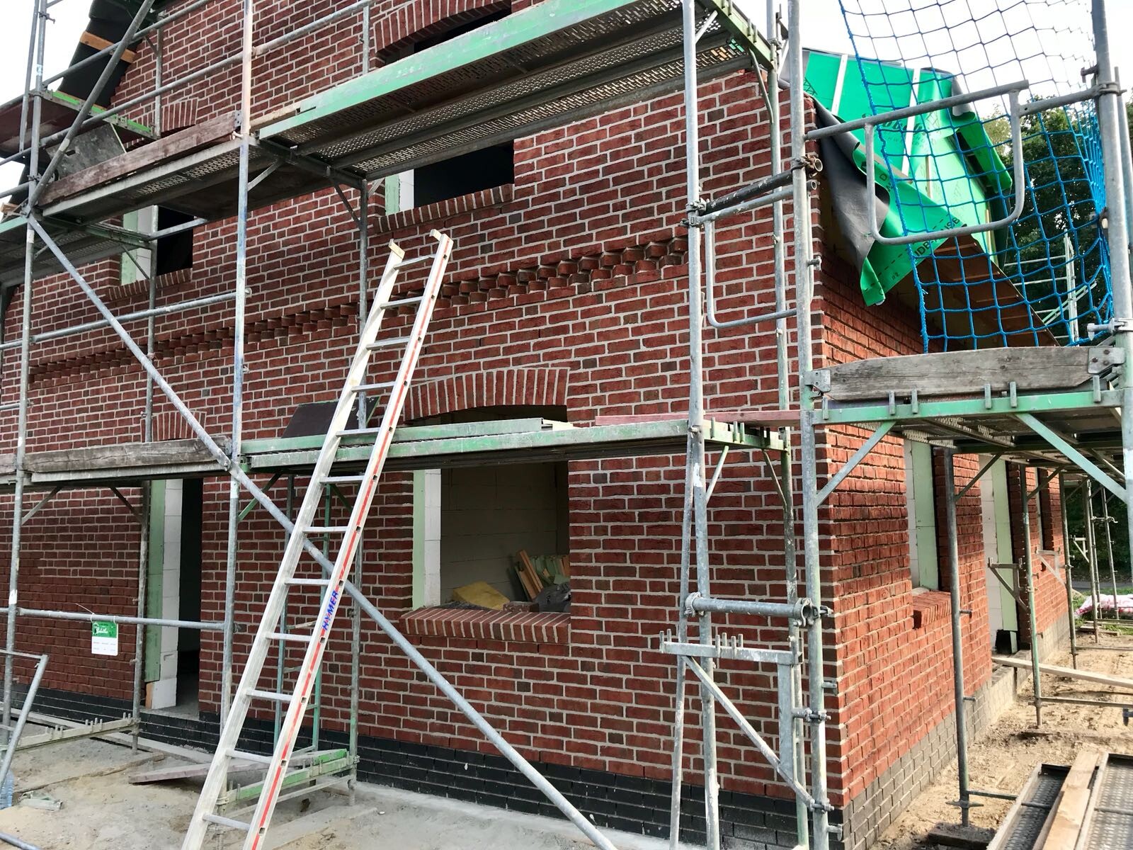 Rotes Backsteingebäude im Bau mit Gerüst, Leiter und Bauplanen auf der Baustelle