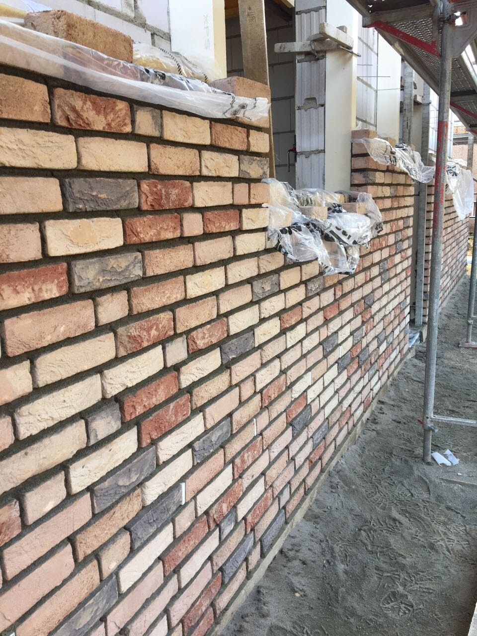 Rohbau: Ziegelwand mit Gerüst und verpackten Ziegeln am Bauplatz