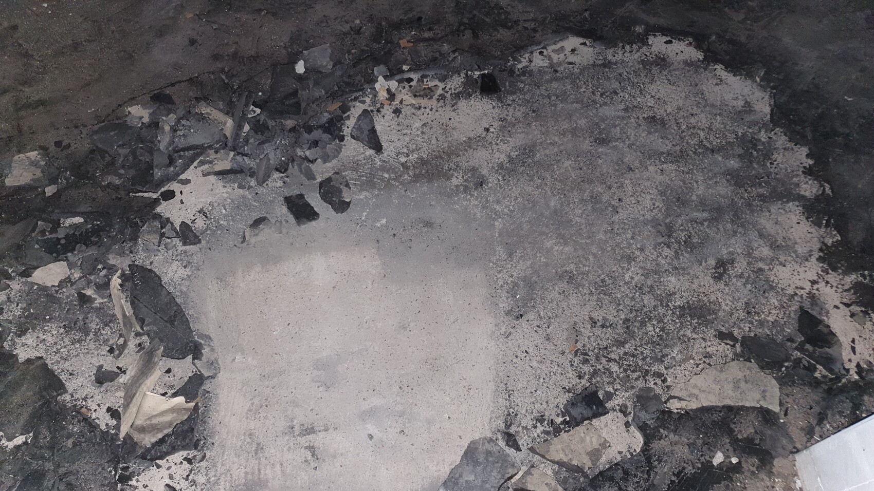 Beschädigte Bodenfläche mit Asche, Bruchsteinresten und dunklen Trümmern.