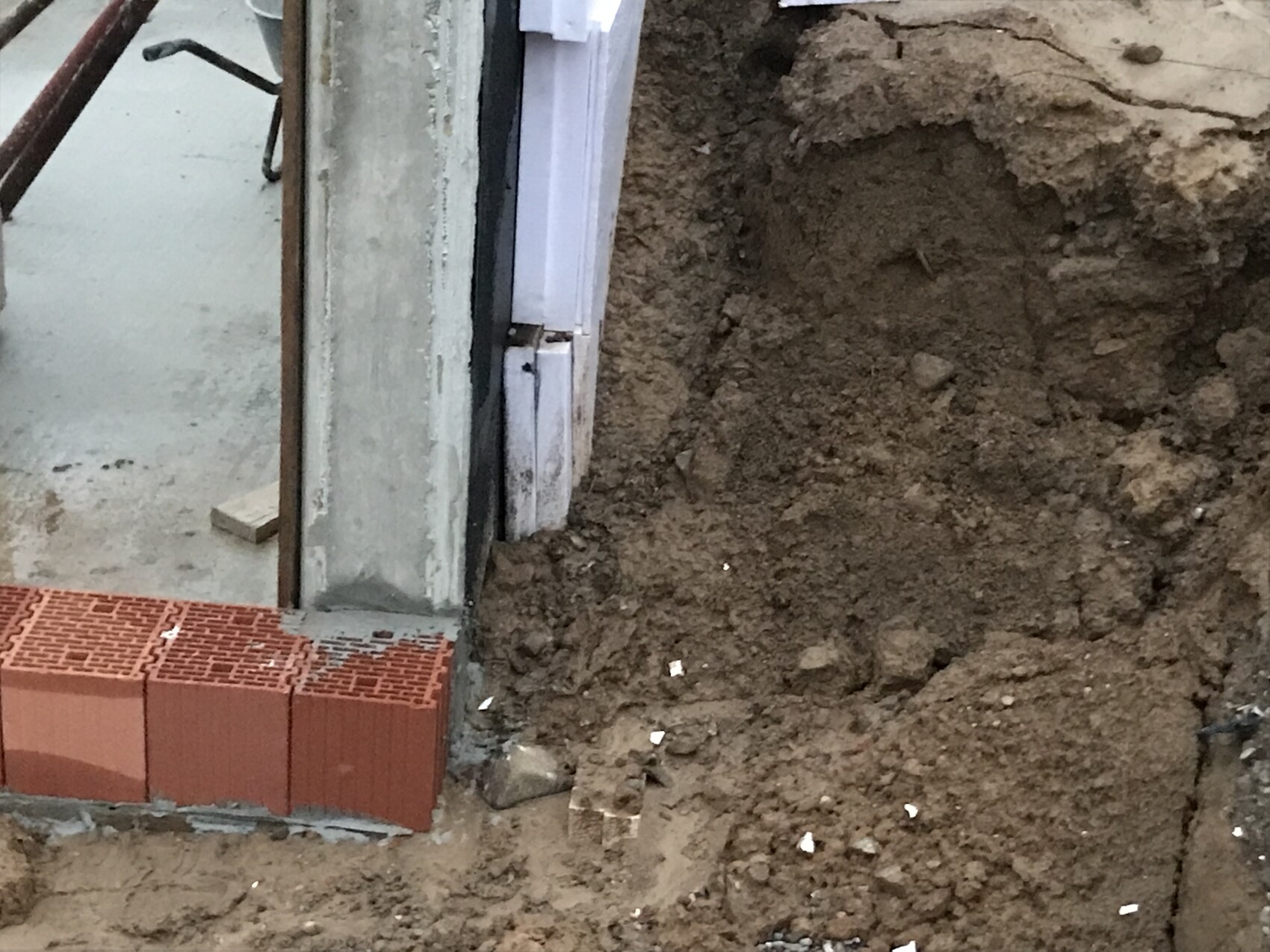 Baustelle: unfertige Türlaibung, rote Lochziegel am Boden, Erdaushub daneben.