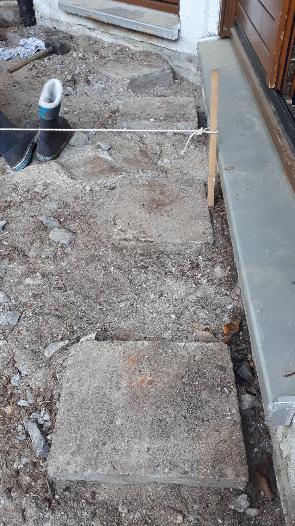 Außenbereich eines Bauvorhabens: Erdarbeiten, Betonstufen, Holzpfosten mit Seil, Stiefel.