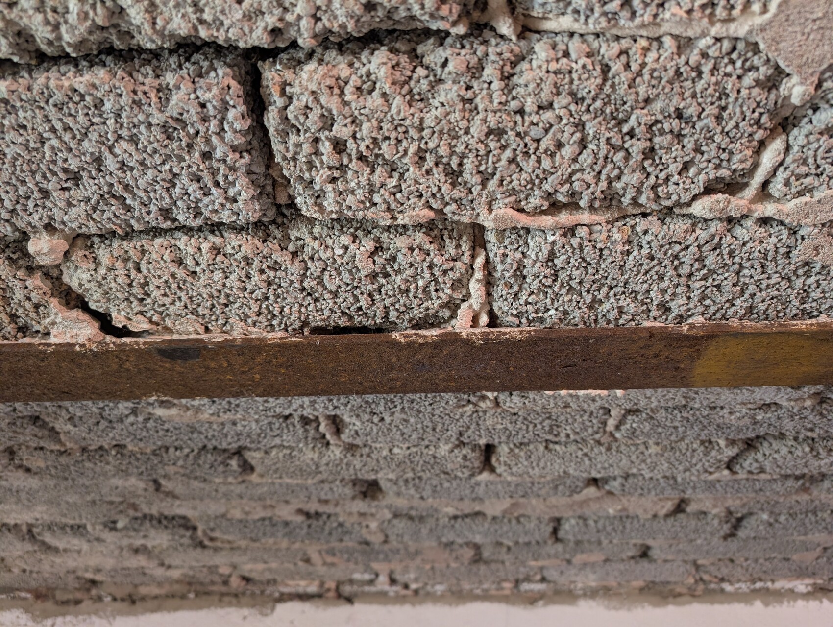 Rohbauwand aus Ziegeln mit rauem Mörtel und rostigem Stahlträger