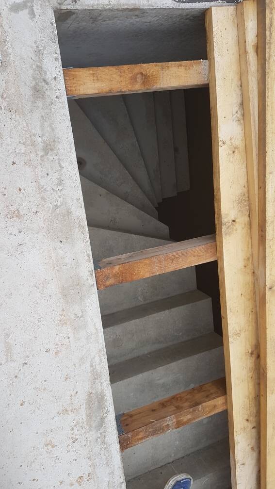 Spiralförmige Betontreppe im Treppenschacht, von Holzbrettern eingerahmt.