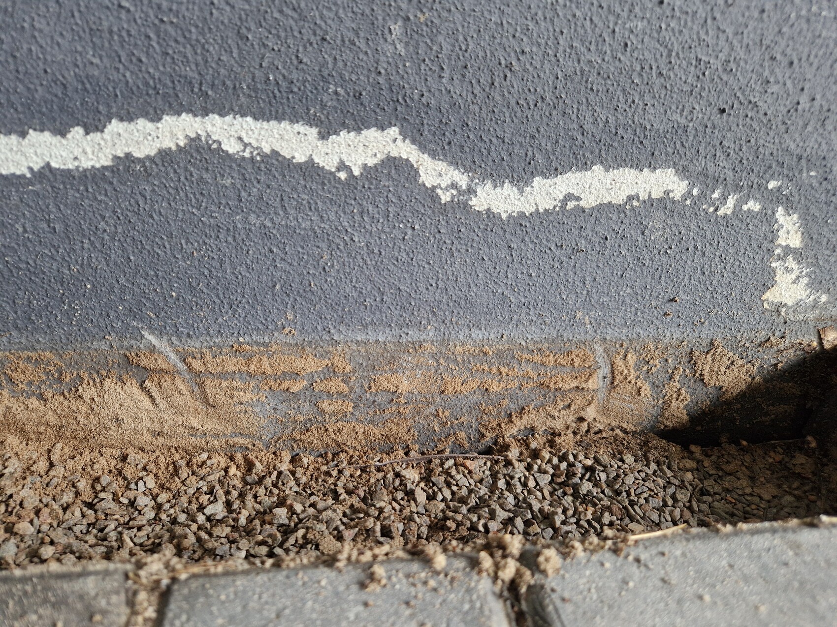 Graue Betonwand mit weißer Linie; Boden aus Kies und Sand.