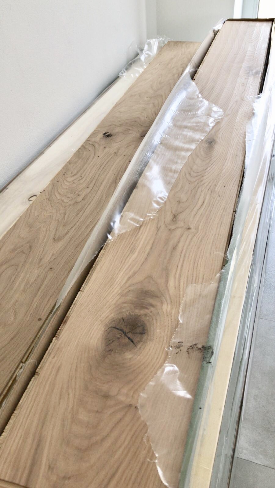 Mehrere lange Holzbohlen liegen an der Wand, teilweise in transparentem Kunststoff verpackt.