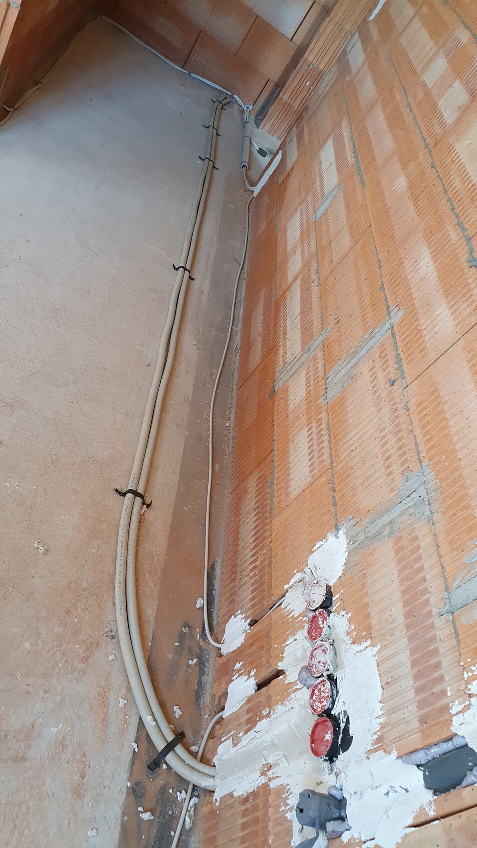 Unfertige Baustelle: Ziegelwand, Kabel und Rohre an der Wandkante.