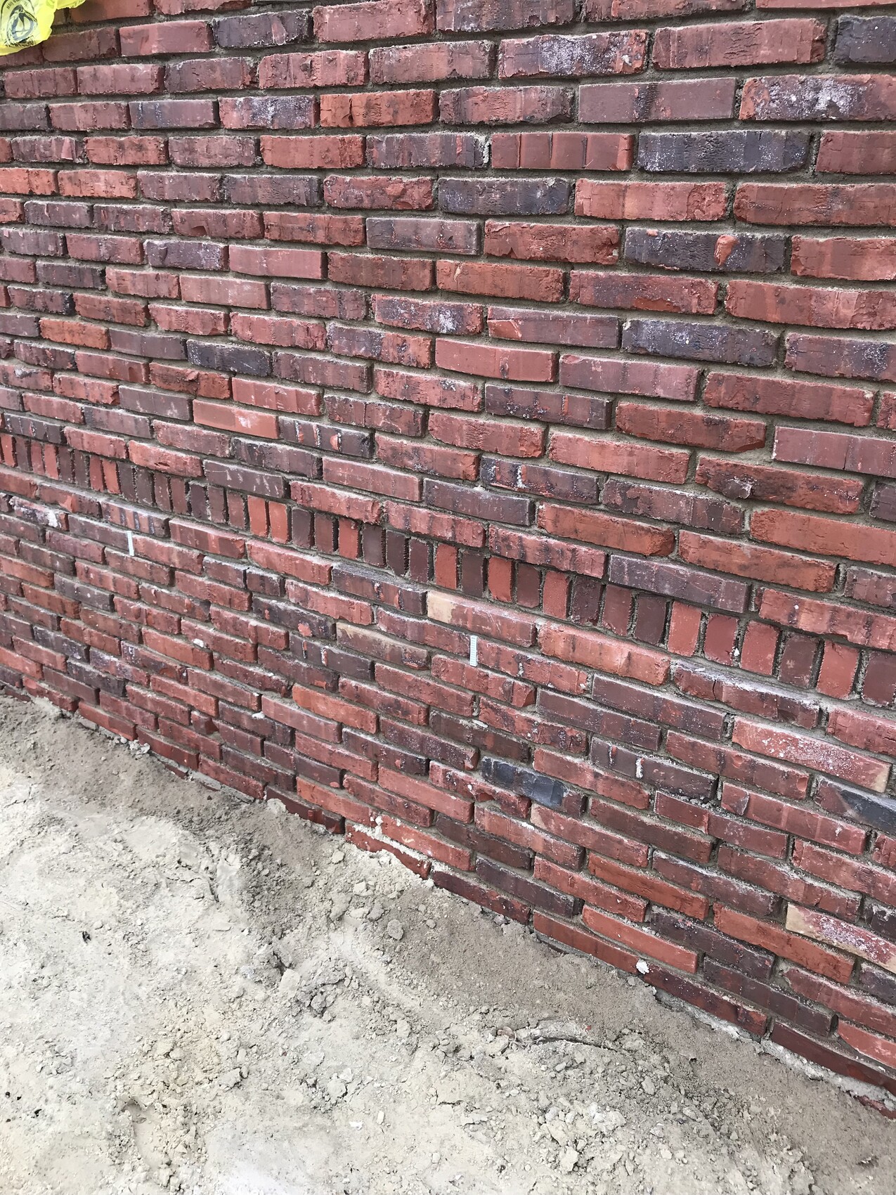Rote Ziegelwand am Baugrund mit losem Erdreich unten.