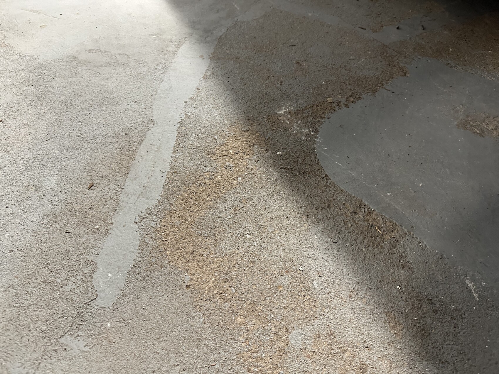 Asphaltboden mit dunkler, kreisförmiger Fläche rechts; daneben liegt Sand entlang der Kante.