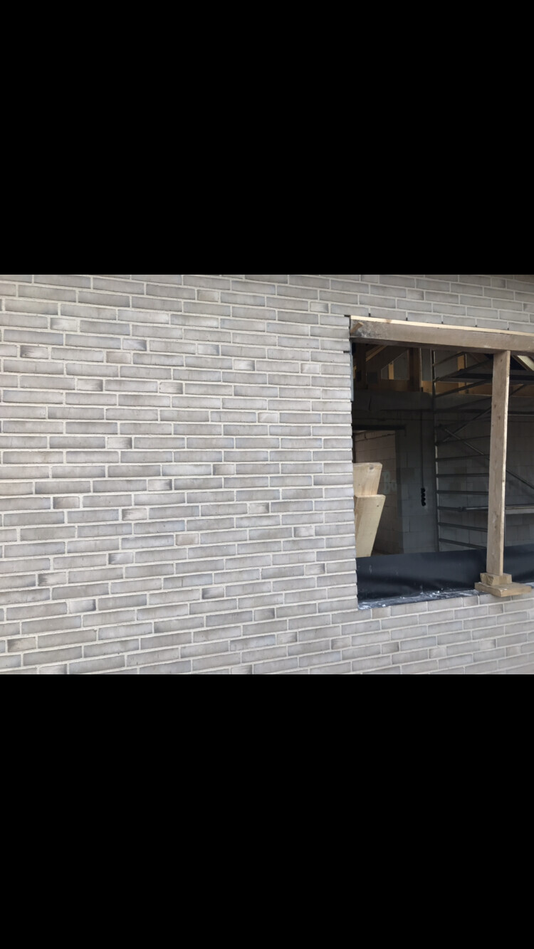 Außenansicht einer grauen Ziegelwand mit offener Fensteröffnung und Holzkonstruktion im Inneren.
