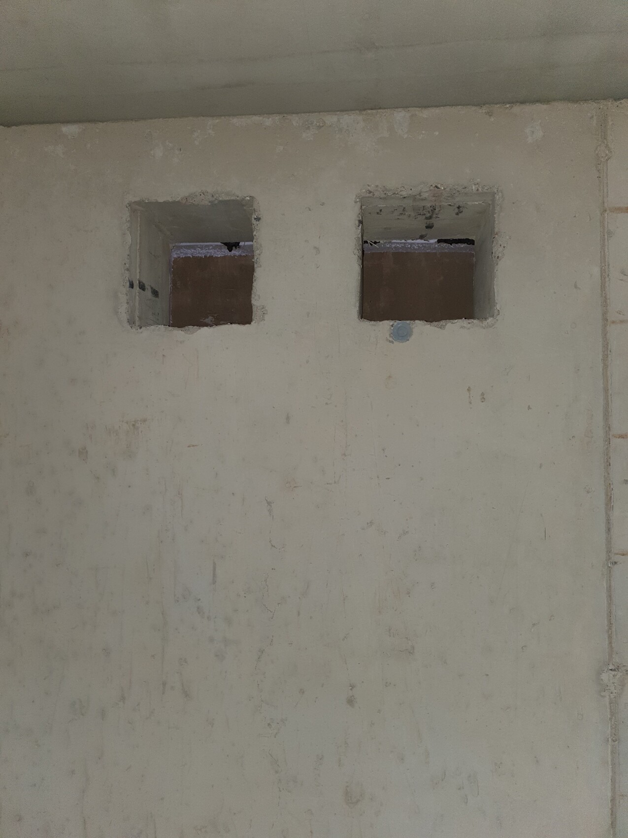 Zwei quadratische Öffnungen in einer rauen Betonwand; dahinter Dunkelheit.