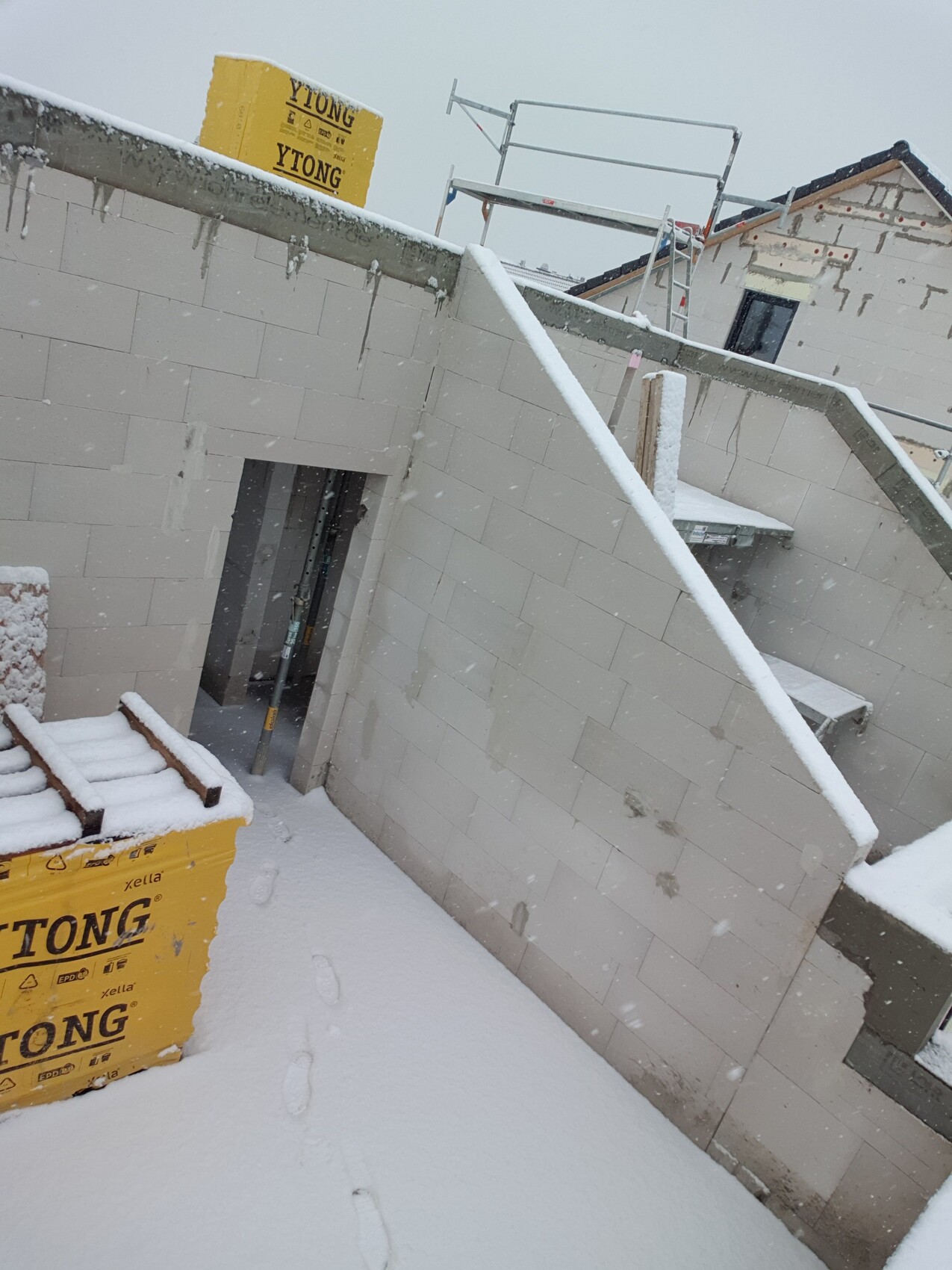 Baustelle im Schnee: Mauerwerk, gelbe YTONG-Platten, Treppe und Gerüst.