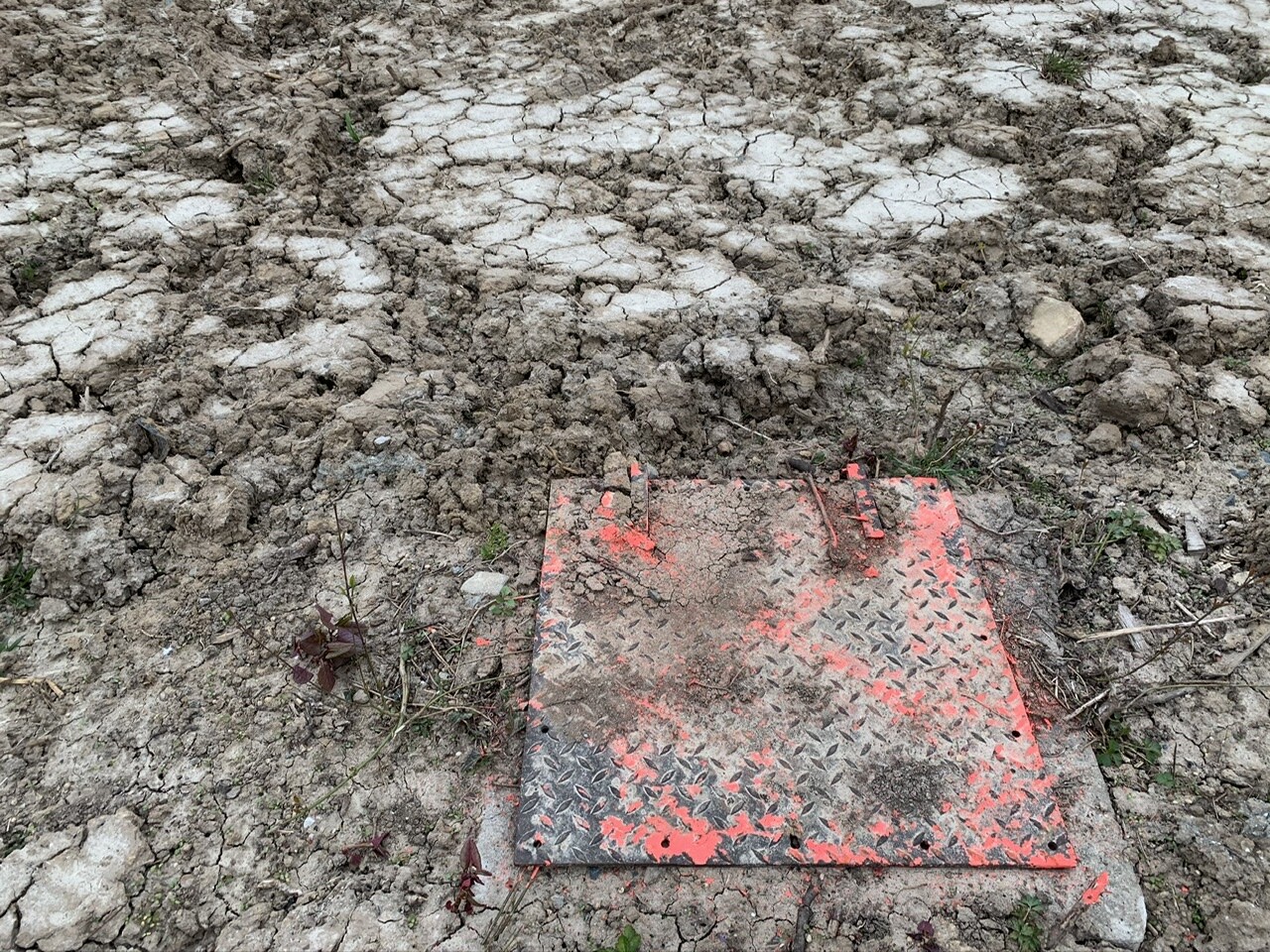 Rissige, trockene Erde mit einer orange bemalten Metallplatte mit Rautenmuster.